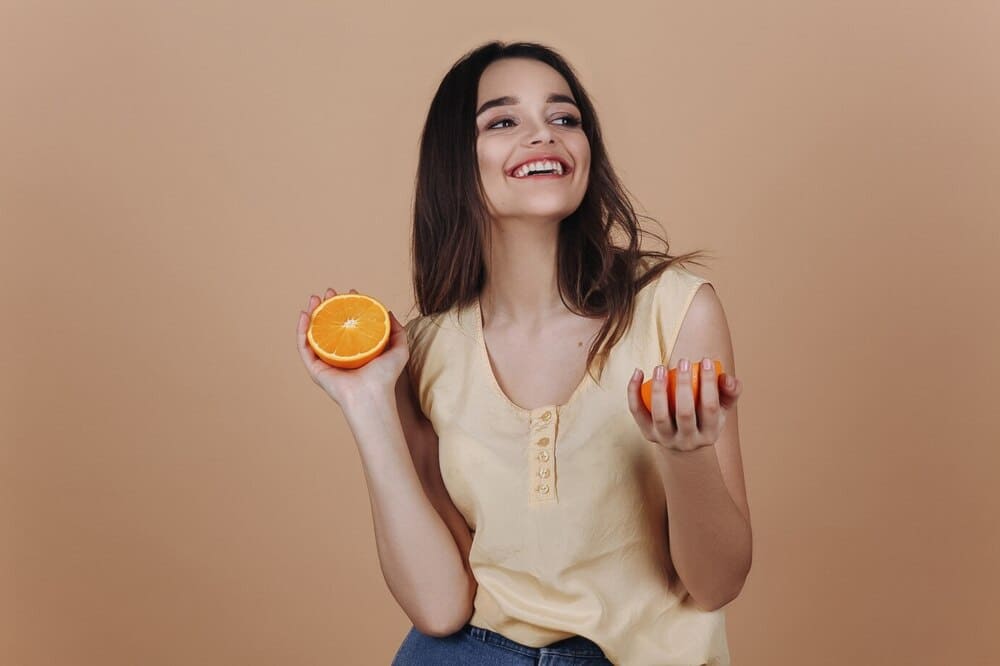 charming-young-woman-with-an-orange-smiles-posing-in-studio