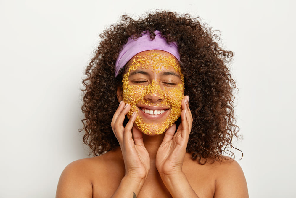 curly-lady-uses-natural-exfoliant-soften-skin-restore-hydration-applies-softnening-sea-salt-facial-scrub-removes-existing-flakes-wears-purple-headband-head-purity