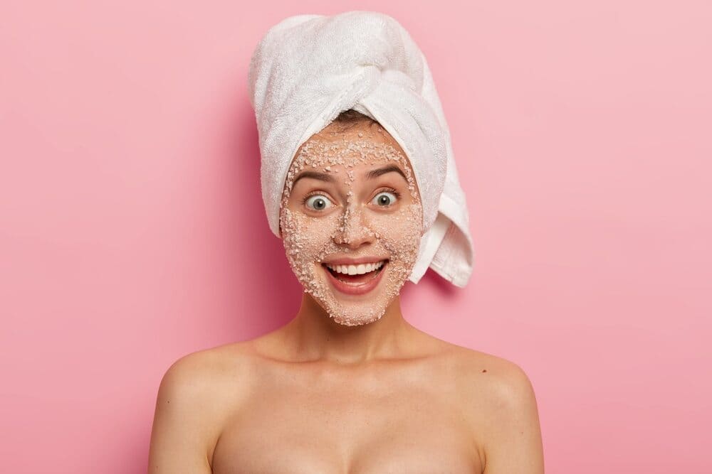 facial-treatment-lovely-and-happy-woman-with-charming-smile-removes-toxins-and-blackheads-from-face-applies-natural-exfoliant-made-of-white-sea-salt-granules-removes-clogs-has-naked-body