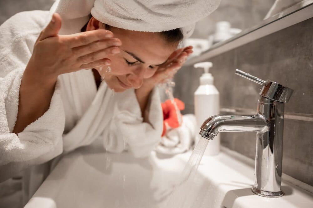 young-beautiful-woman-in-the-bathroom-with-a-towel-on-her-head-washes-her-face-with-tap-water